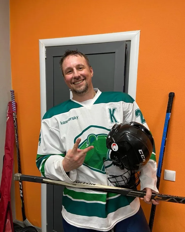 Alex in an ice hockey jersey holding a helmet and stick